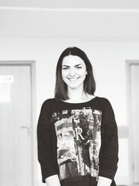 Portrait of smiling young woman standing against wall