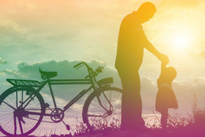 People riding bicycle against sky during sunset