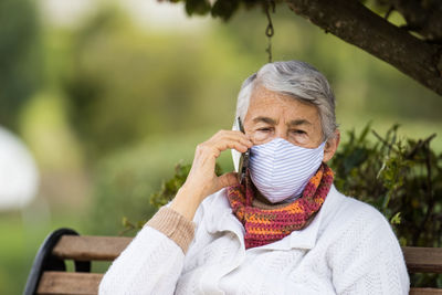 Senior woman wearing mask talking on phone outdoors