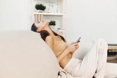 Young woman using mobile phone while sitting on bed at home