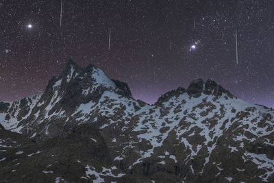 Scenic view of dark mounts with snow and rough peaks under starry sky at dusk