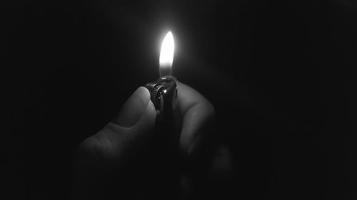 Close-up of hand holding lit candle in darkroom
