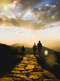 People walking on road against sky during sunset