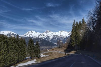 Road amidst trees and snowcapped mountains against sky