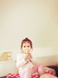Girl eating ice cream while sitting against wall at home