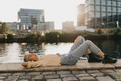 Side view of woman sitting on retaining wall next to the water