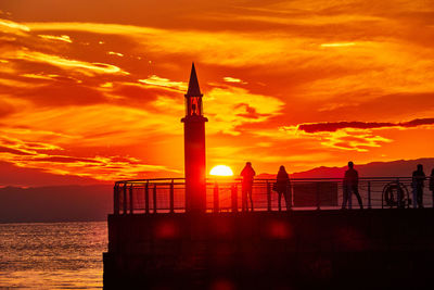 Scenic view of sea with silhouette people and lighthouse against sky during sunset