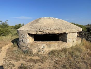 Old abandoned building on field against clear blue sky