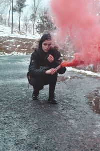 Full length portrait of woman holding distress flare on road