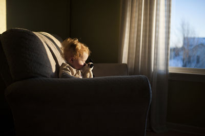Baby boy playing with toy while sitting on couch at home during sunset