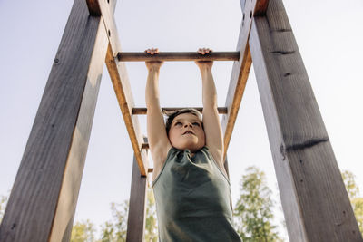 Low angle view of determined boy hanging while doing monkey bars at summer camp