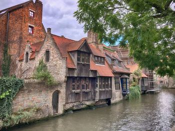 Houses by river amidst buildings against sky