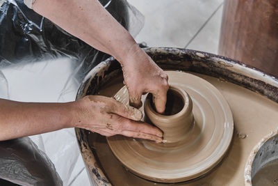 Hands of senior woman sculpting clay vase on potter's wheel.