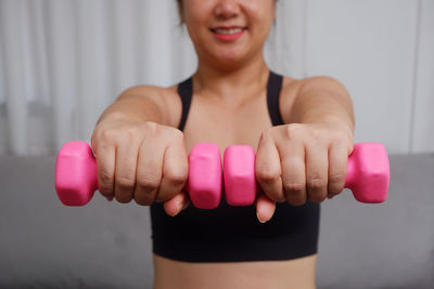 Midsection of woman lifting dumbbell in gym