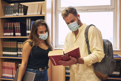 A young couple wearing a mask check out a library book