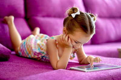 Girl using digital tablet while lying on sofa at home