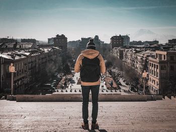 Rear view of man with backpack standing on buildings against sky