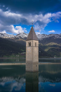 Reflection of tower on lake against mountains