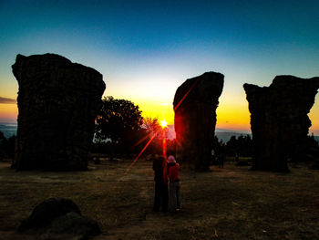 Rear view of people on field against clear sky during sunset
