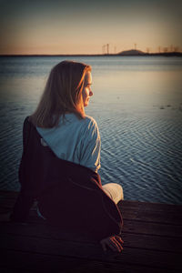 Rear view of girl looking at lake against sky during sunset