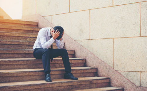 Full length of man sitting on staircase against wall