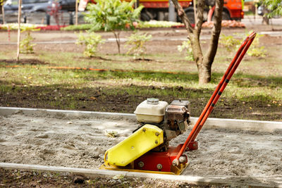 An old petrole platecompactor for compacting sandy soil stands on a sandy path under construction