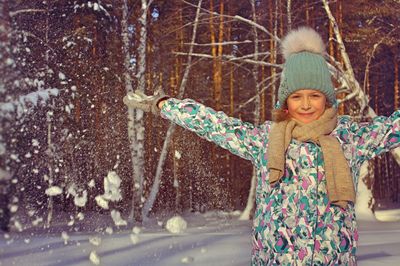 Portrait of smiling girl with arms outstretched standing in snow covered forest