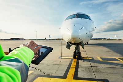 Cropped hands of man using digital tablet against airplane at runway