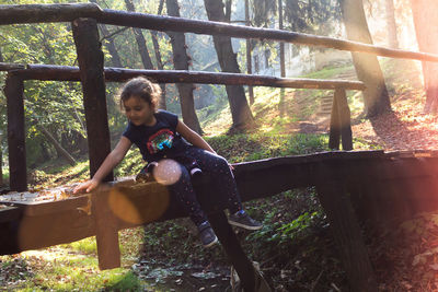 Portrait of teenage girl sitting on tree in forest