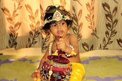 Baby boy dressed as krishna holding decorated handi at home
