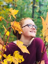Smiling young woman by leaves during autumn