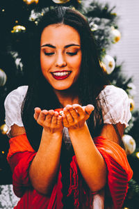 Smiling young woman holding ornament against christmas tree