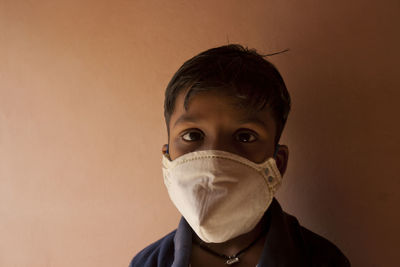 Portrait of boy wearing flu mask standing against wall
