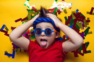 Child a boy in a red t shirt and sunglasses is lying on yellow paper resting at home