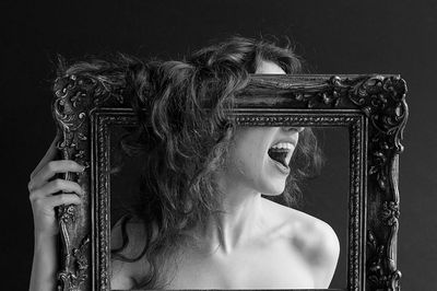 Close-up of shirtless woman screaming while holding frame against black background