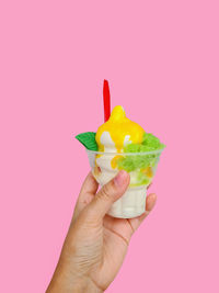 Cropped hand holding ice cream cone against yellow background