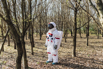 Astronaut wearing space suit and helmet looking away in forest