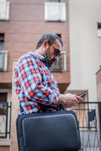 Portrait of handsome businessman with sunglasses and plaid shirt walking  and typing messages