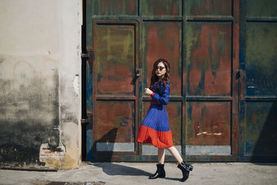 Full length portrait of young woman walking against metallic gate