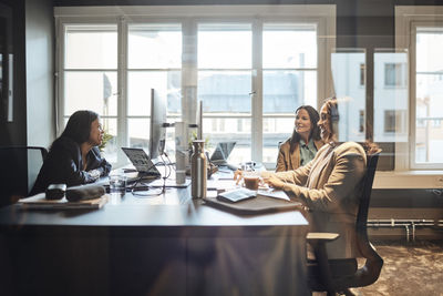 Multiracial female business colleagues discussing strategy while sitting at desk in office