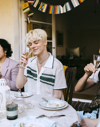 Smiling gay man smelling wine while sitting at table during dinner party in back yard