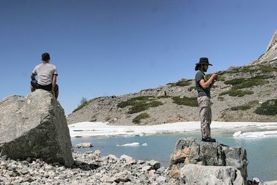 Male hikers hiking by lake against clear blue sky during sunny day