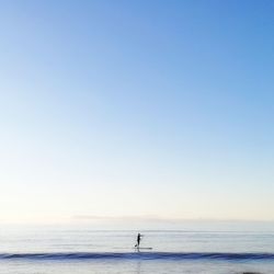 Man paddleboarding in sea against clear sky