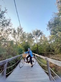 Man riding bicycle on footbridge against sky
