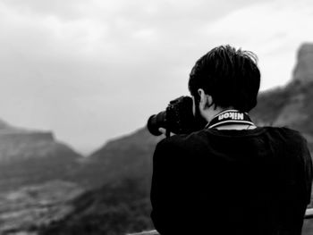 Rear view of man looking at mountains against sky