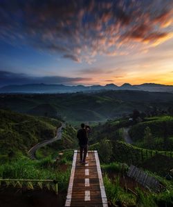 Rear view of man standing against mountains during sunset