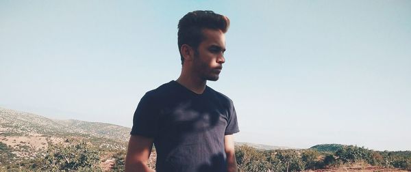 Young man standing on landscape against clear sky