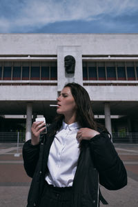 Young woman looking away while standing against built structure