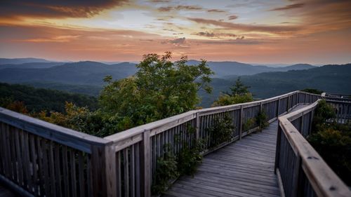 Empty boardwalk against mountains during sunset