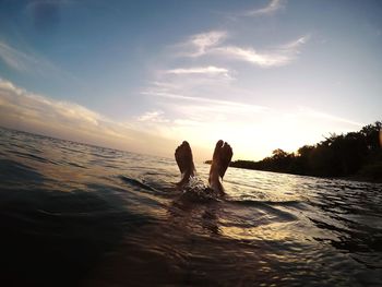 Low section of person in sea during sunset